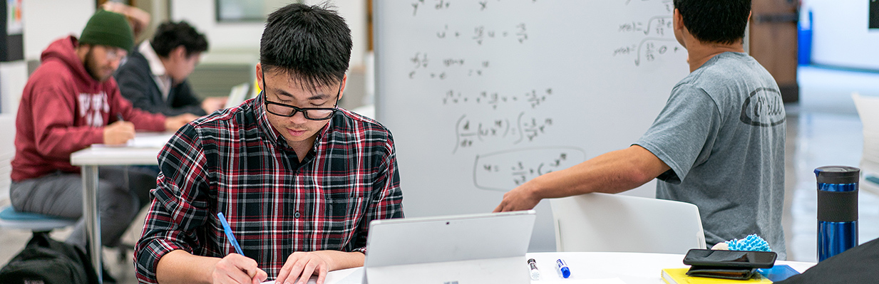 Two students working on a computer and whiteboard.